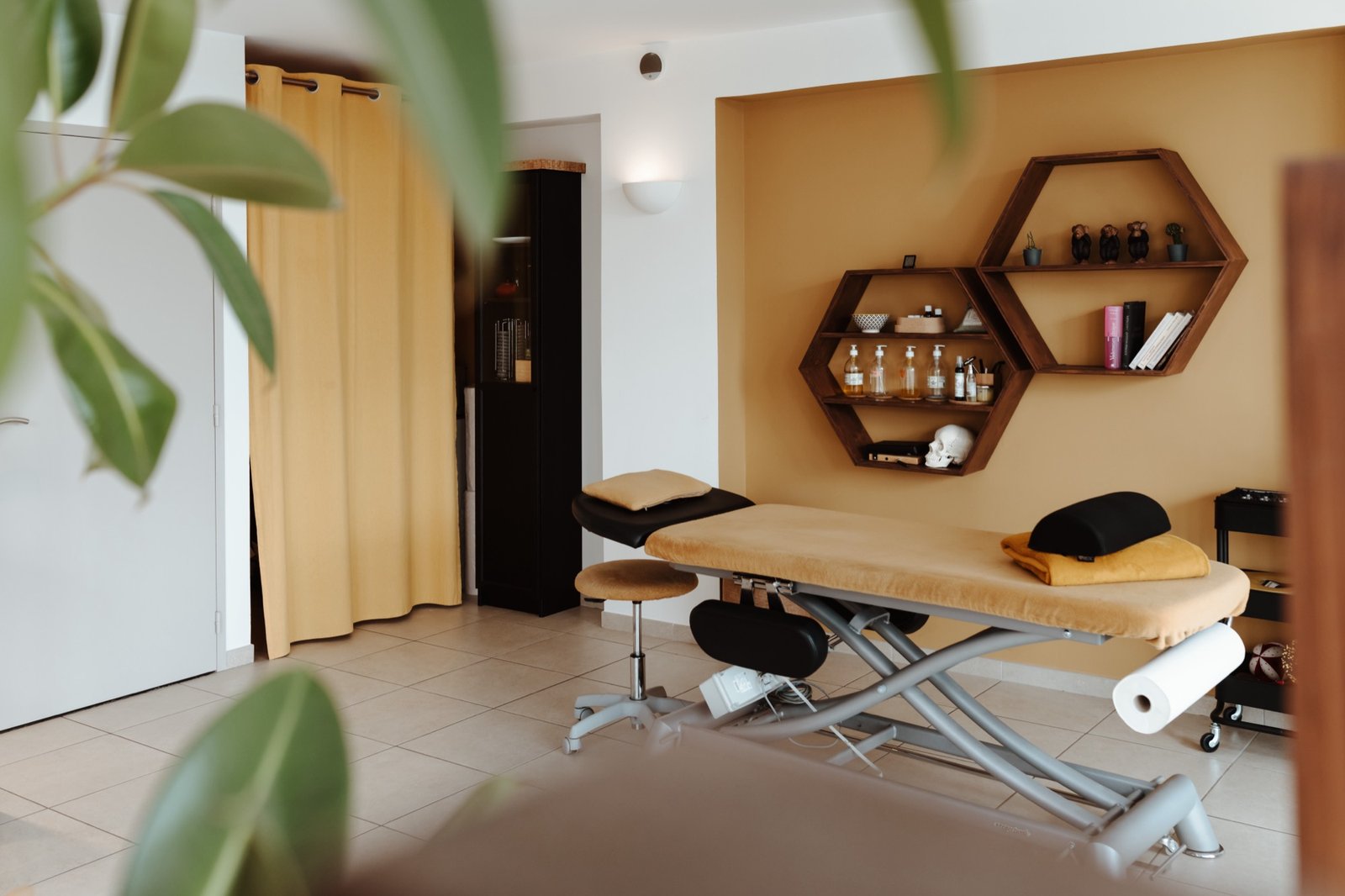 Duo Ostéo Crestet : Salle de soin aux murs ocre, table d'ostéopathie et étagères hexagonales