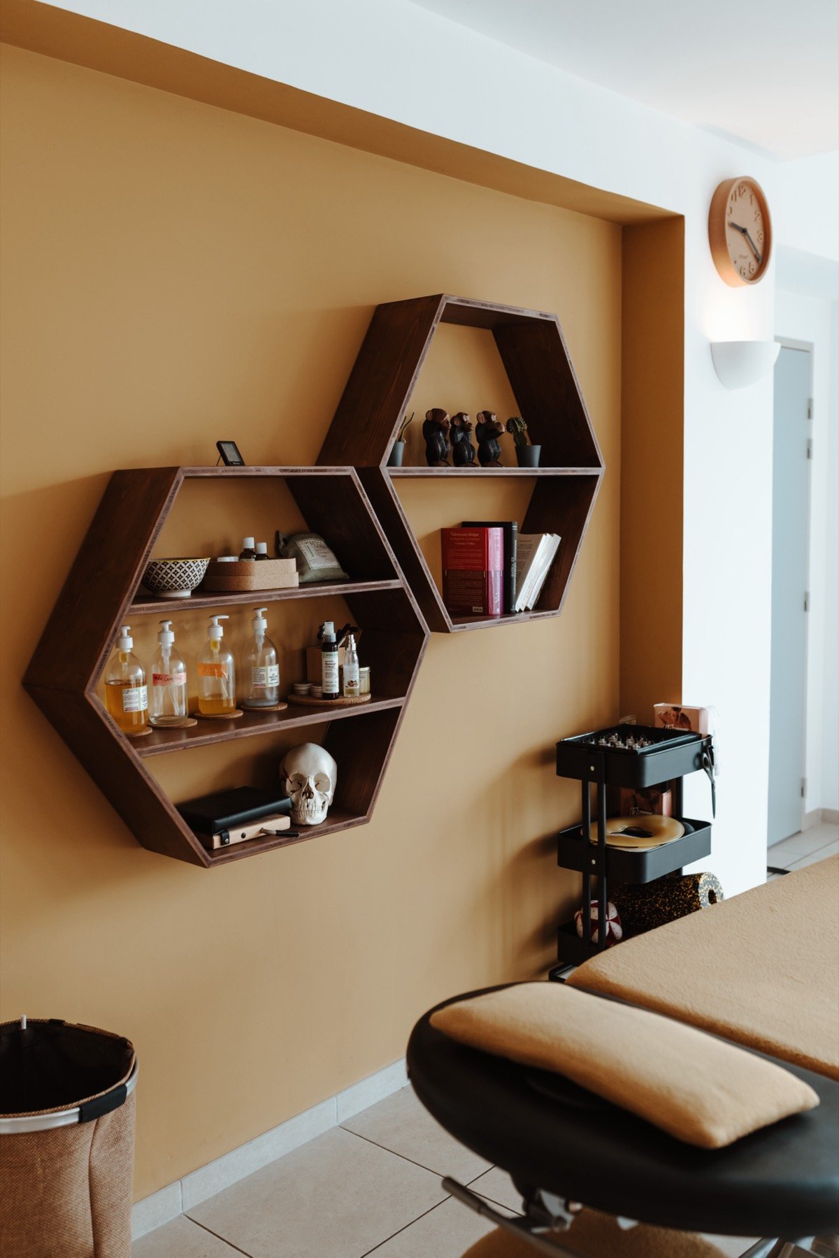 Salle de soin du cabinet Duo Ostéo du Crestet : table d'ostéopathie, niche ocre et étagères hexagonales en bois