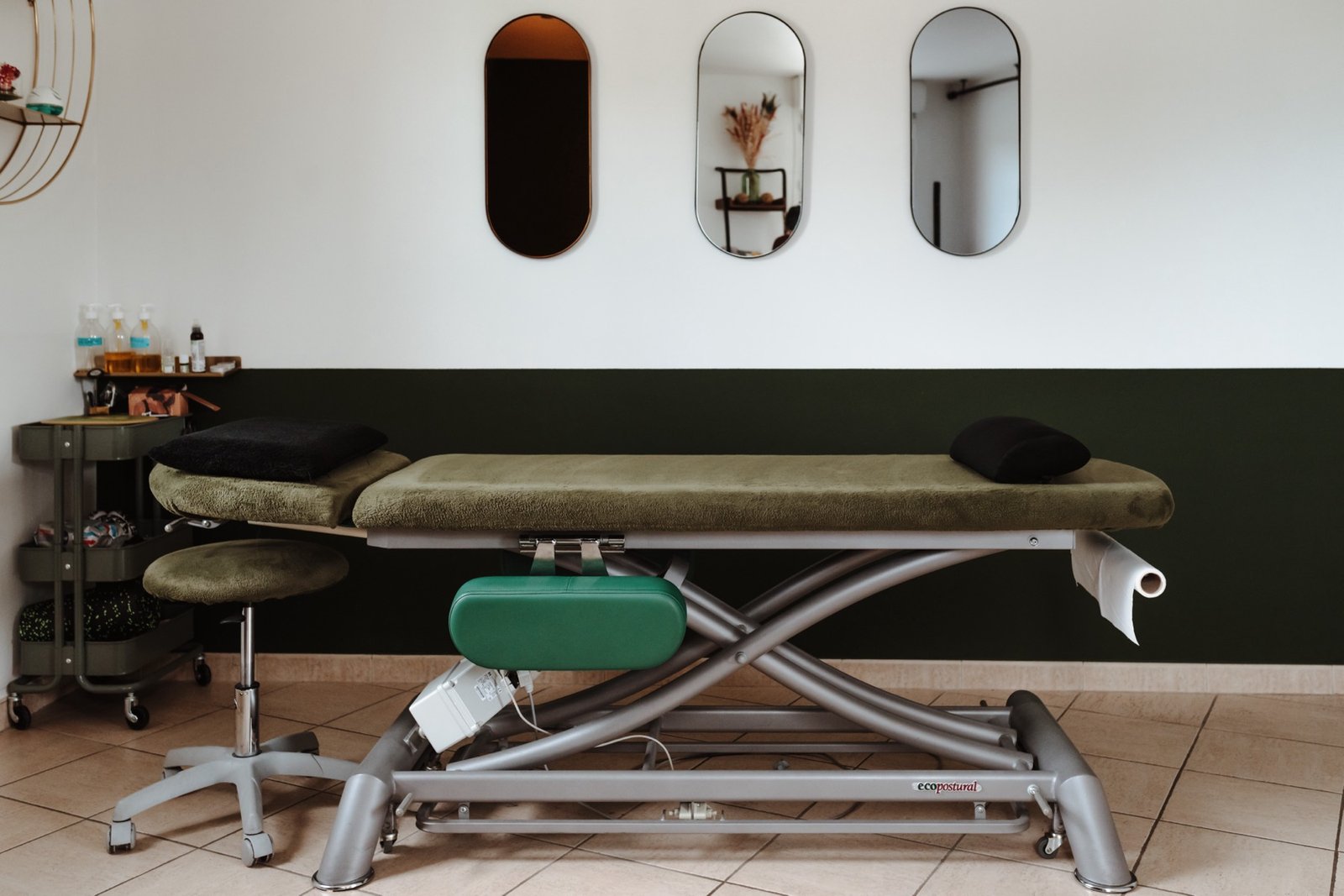 Salle de soin du cabinet Duo Ostéo de Vaison-la-Romaine : table d'ostéopathie, miroirs ovales et mur vert sapin